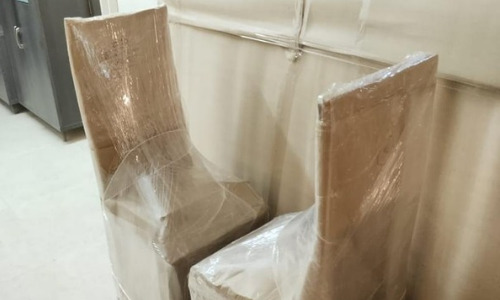 High-back dining chairs covered in brown packing paper and plastic sheets by the best packers and movers team