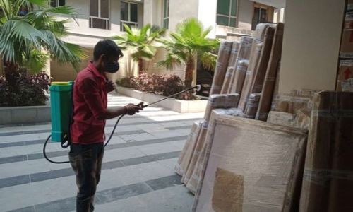 Worker sanitizing wrapped cargo boxes with a spray machine, a safety step by the best packers and movers