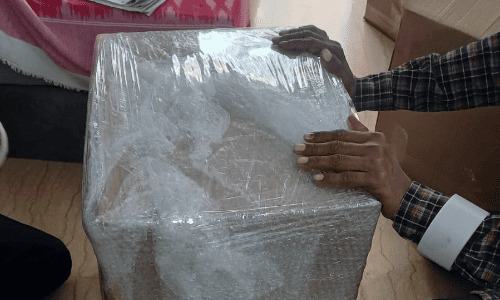 Movers and packers applying stretch film by hand onto a parcel during a packing job