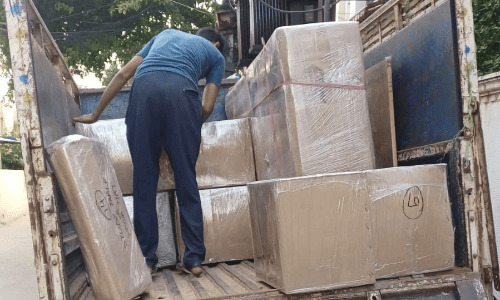 Crew member arranging film-wrapped wooden furniture inside the cargo area of a packers movers vehicle
