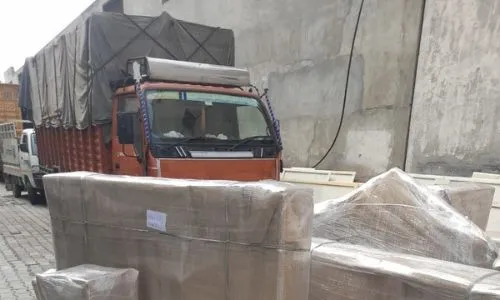 Heavy furniture securely wrapped in cardboard and plastic stretch film, lined up next to a transport truck by euro packers movers kolkata for safe loading.