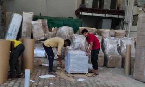 Shifting crew sorting and wrapping household items inside a spacious industrial storage terminal operated by packers movers kolkata. 